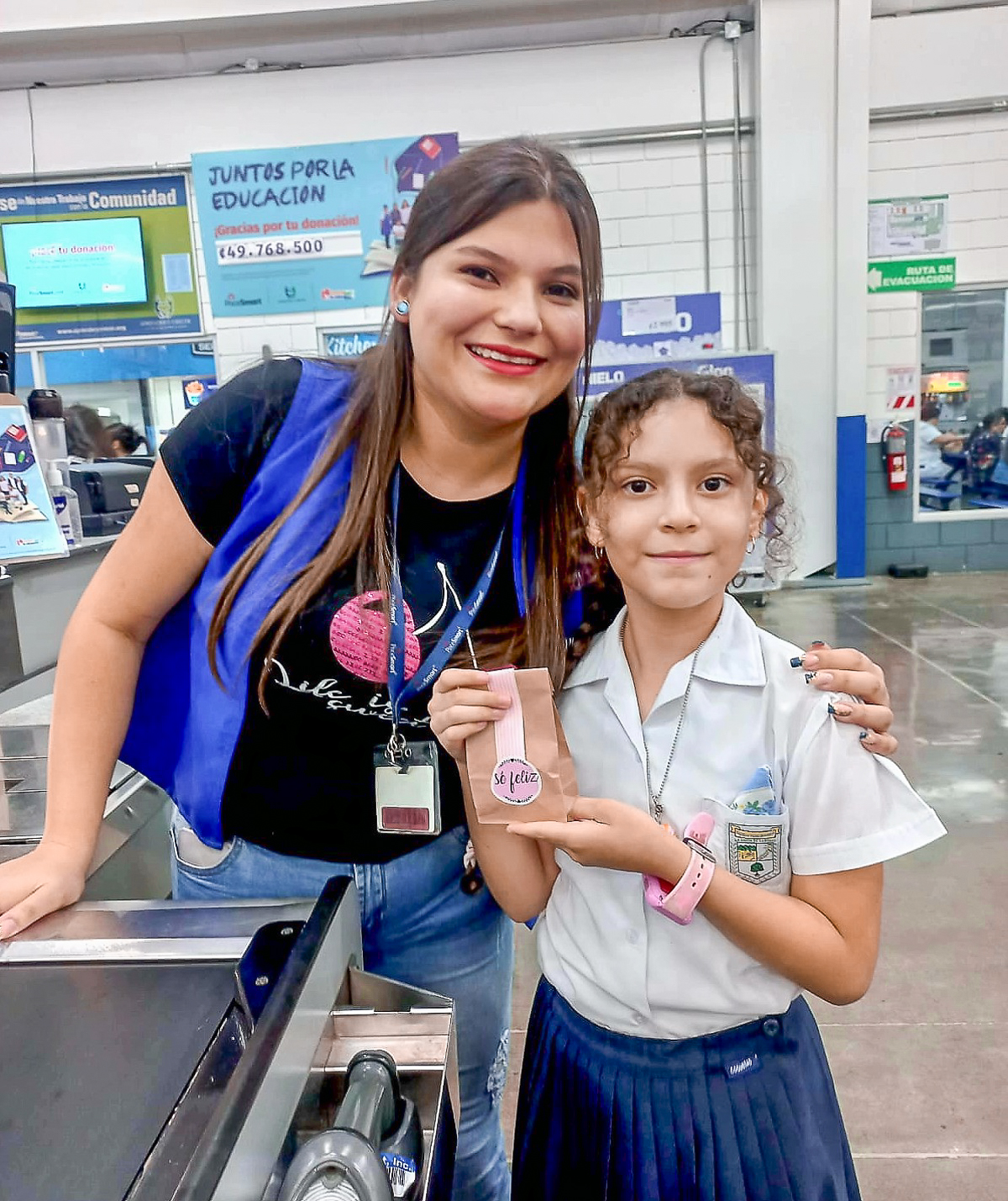 PriceSmart cashier posing next to a student holding a "Be Happy" bag