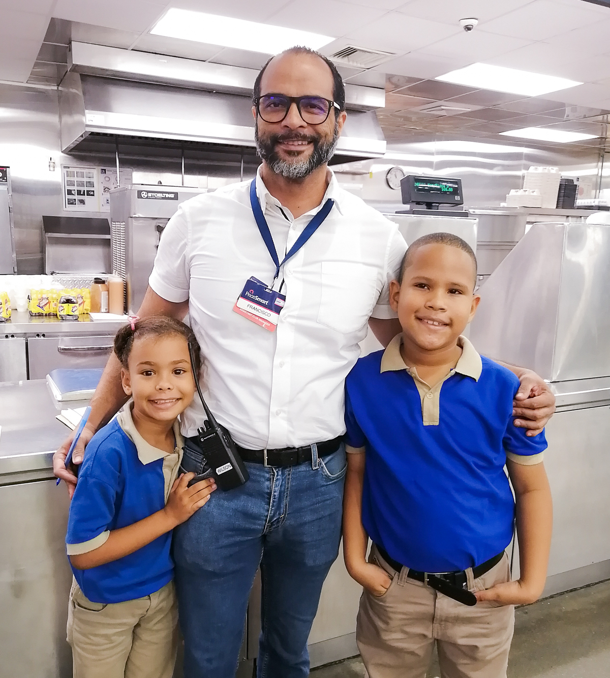 PriceSmart employee posing next to two elementary school students
